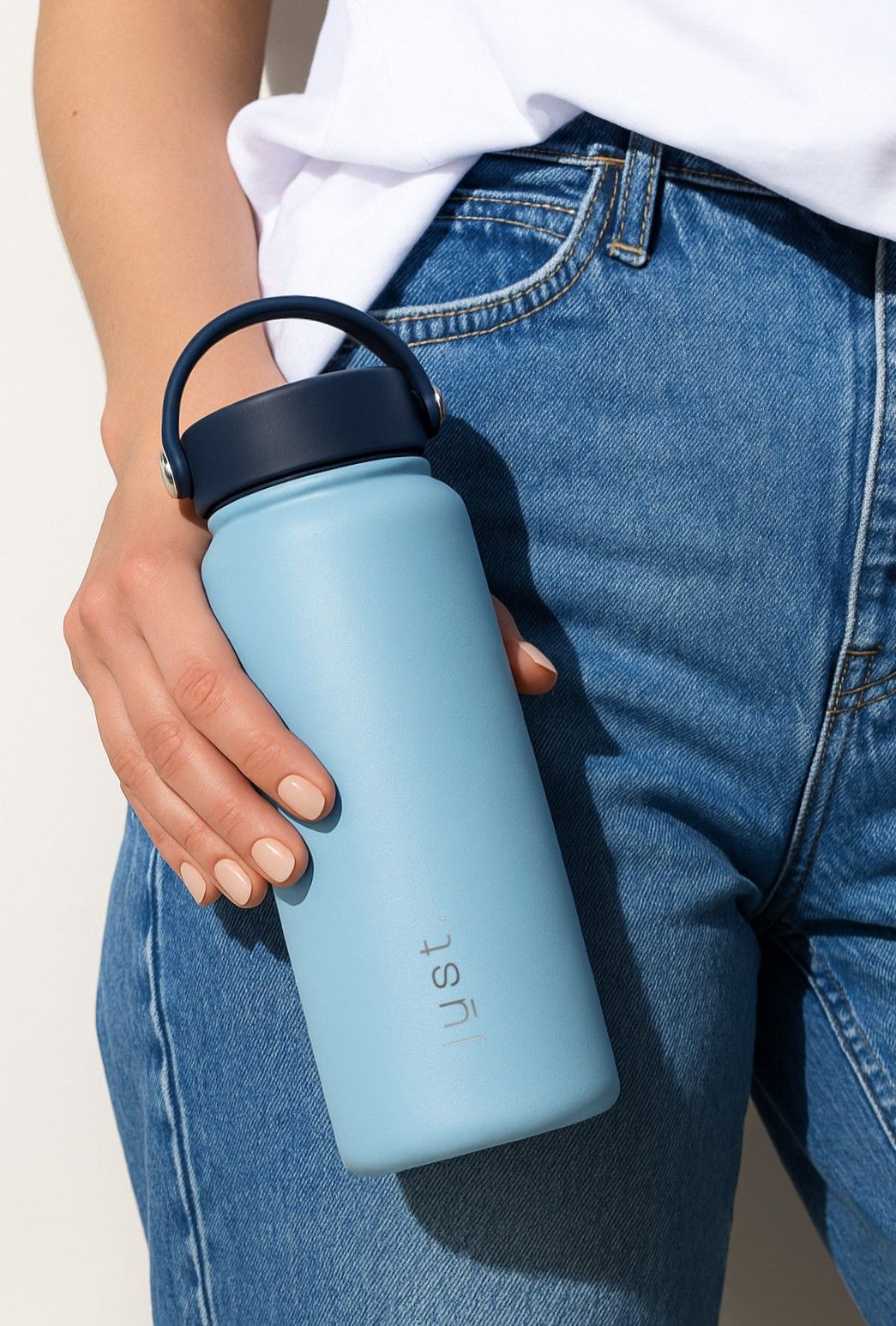 Person holding a light blue water bottle with a dark blue lid, wearing blue jeans and a white shirt.