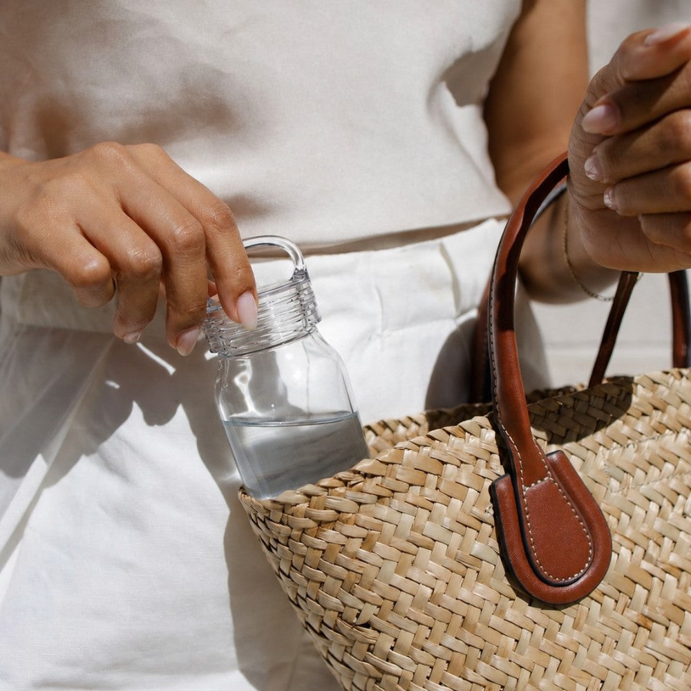 Person putting a small glass water bottle in a handbag