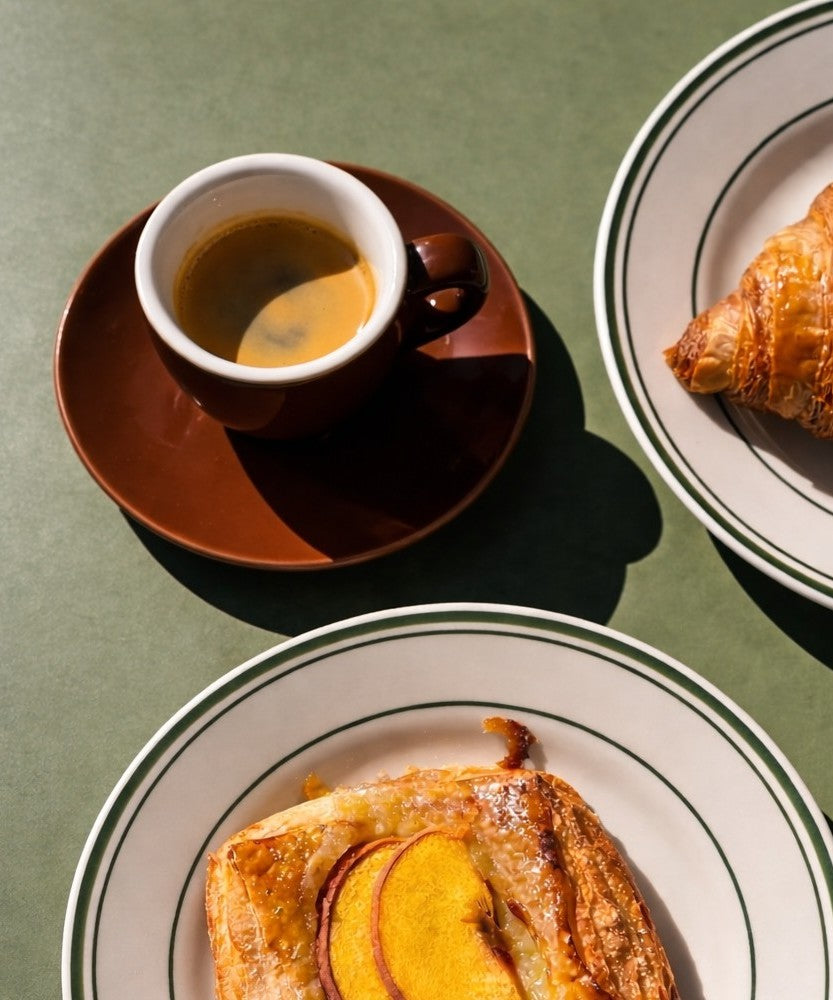 Cup of espresso on a saucer with pastries on plates against a green background