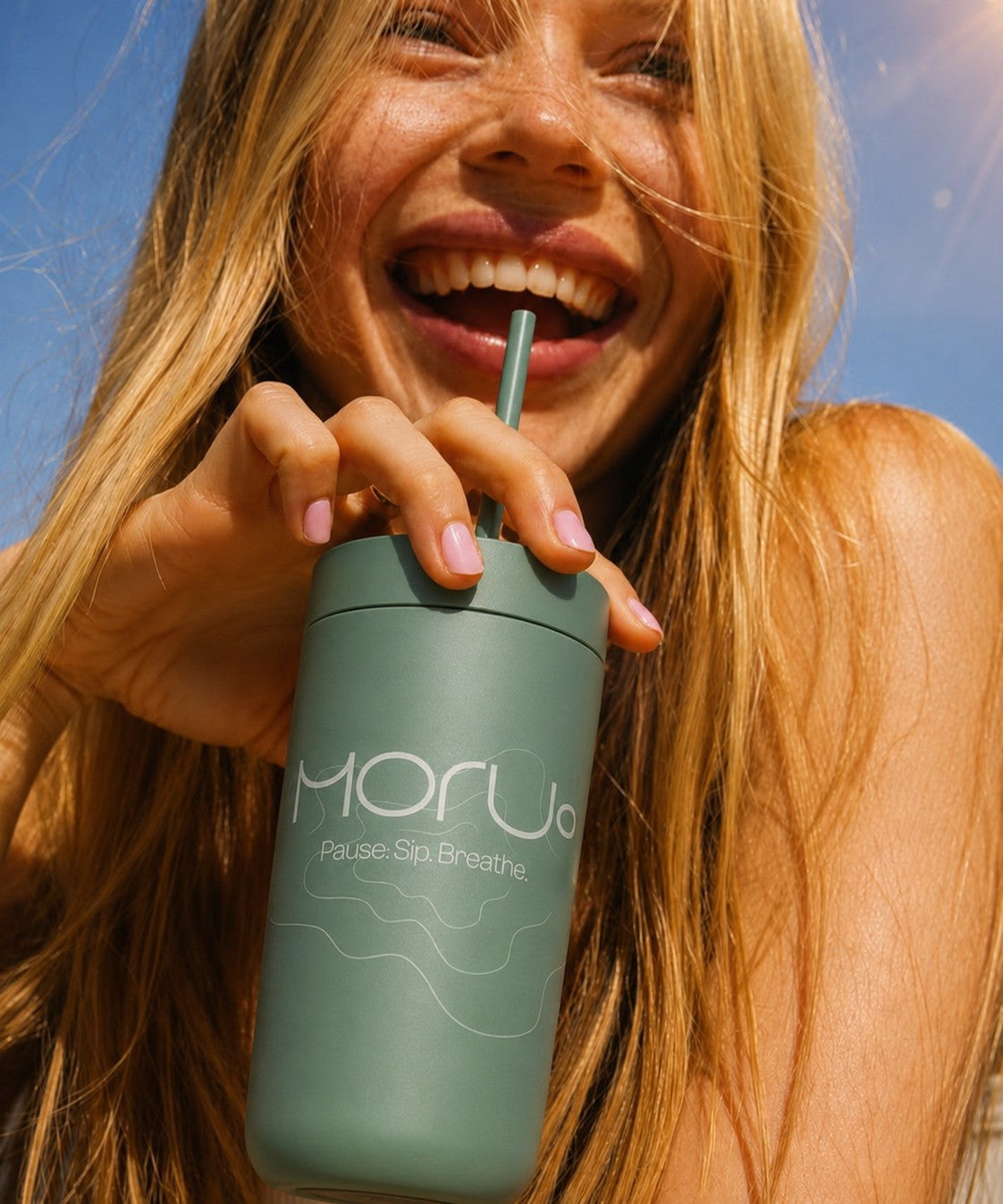 Lady sipping from a green custom branded tumbler with a straw lid, with a bright sunny background