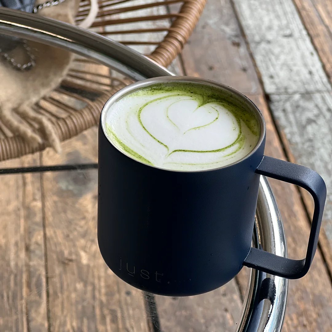 blue reusable coffee mug with matcha latte inside, on a glass table