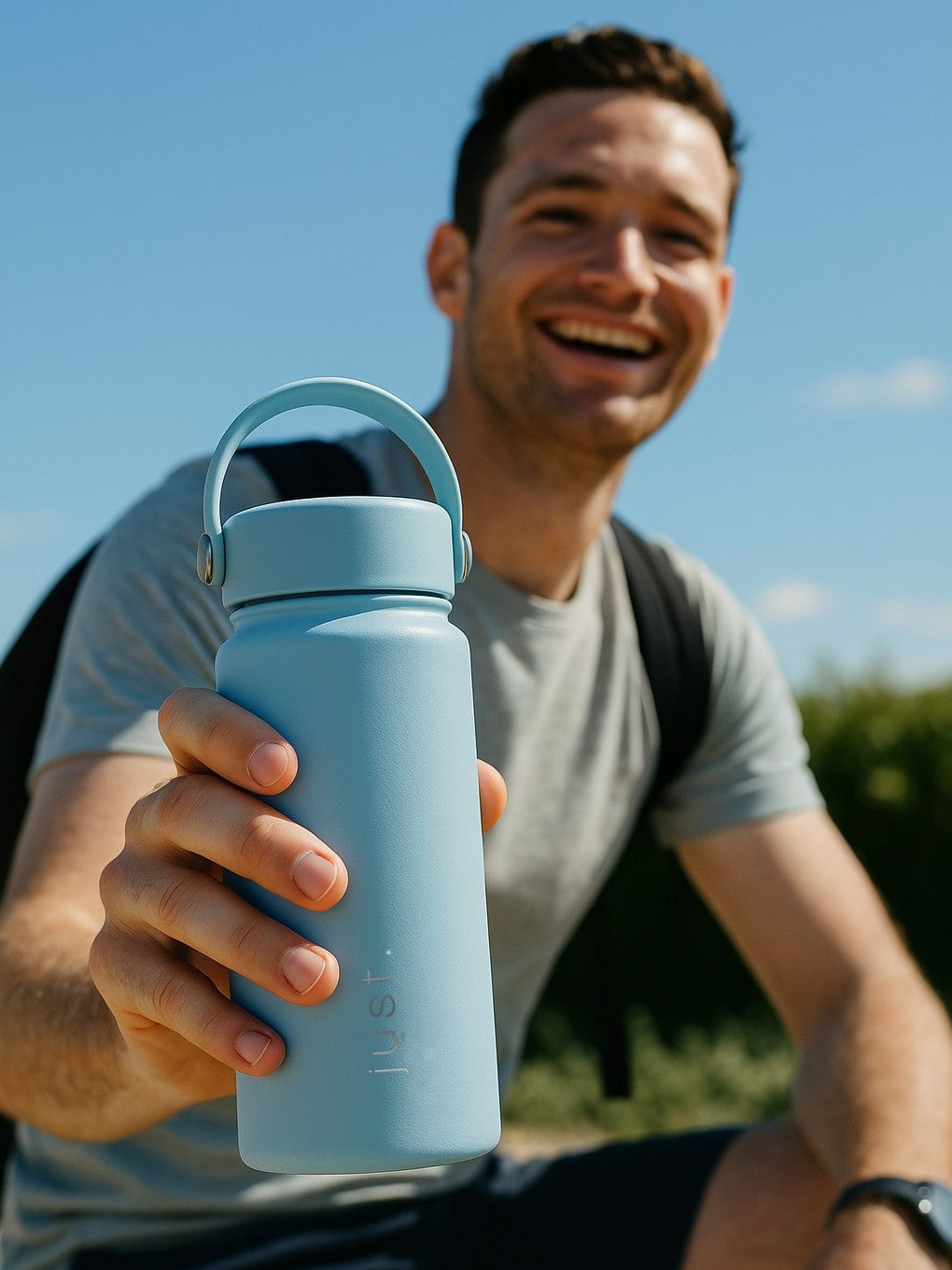 Man holding a light blue water bottle outdoors with a clear sky background
