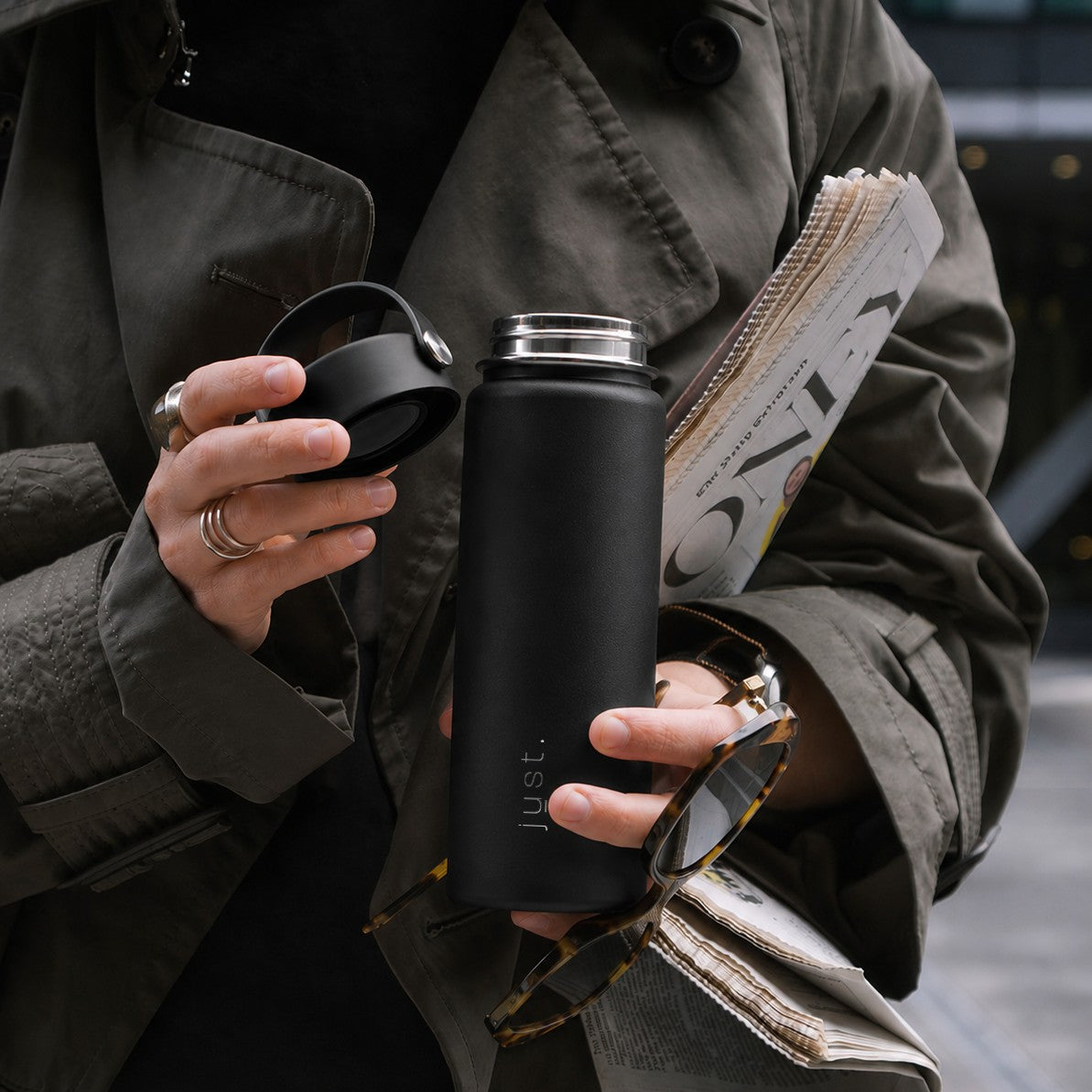 Person holding a black reusable water bottle from Just Bottle