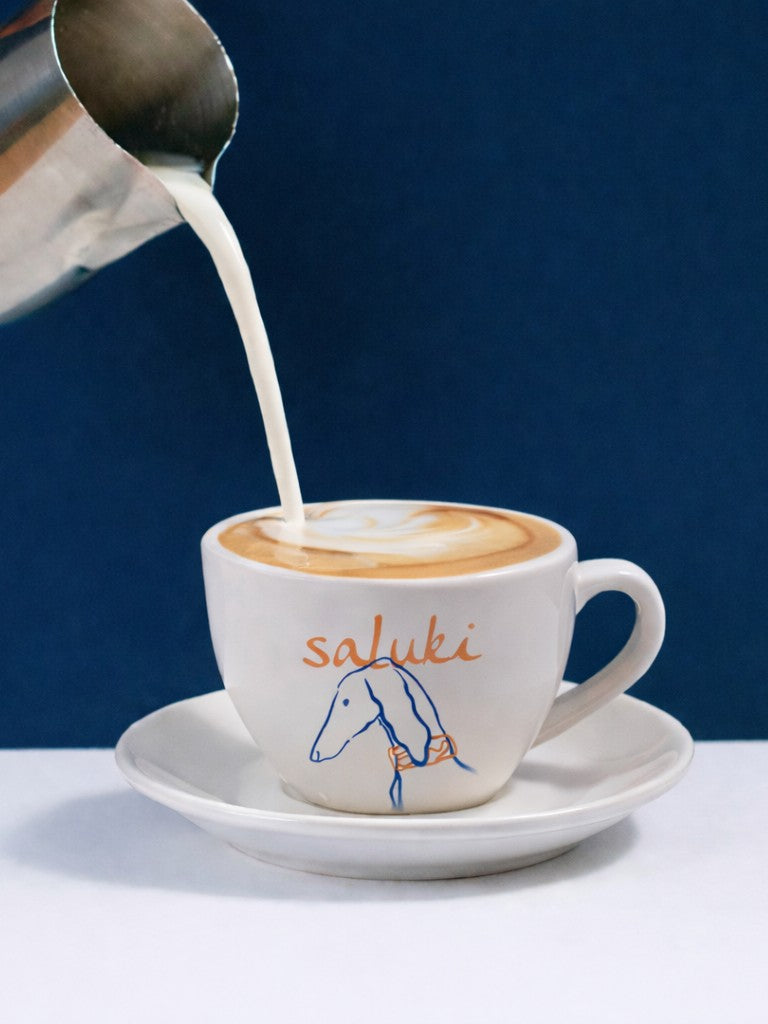 Cup of coffee with custom design being topped with milk against a blue background