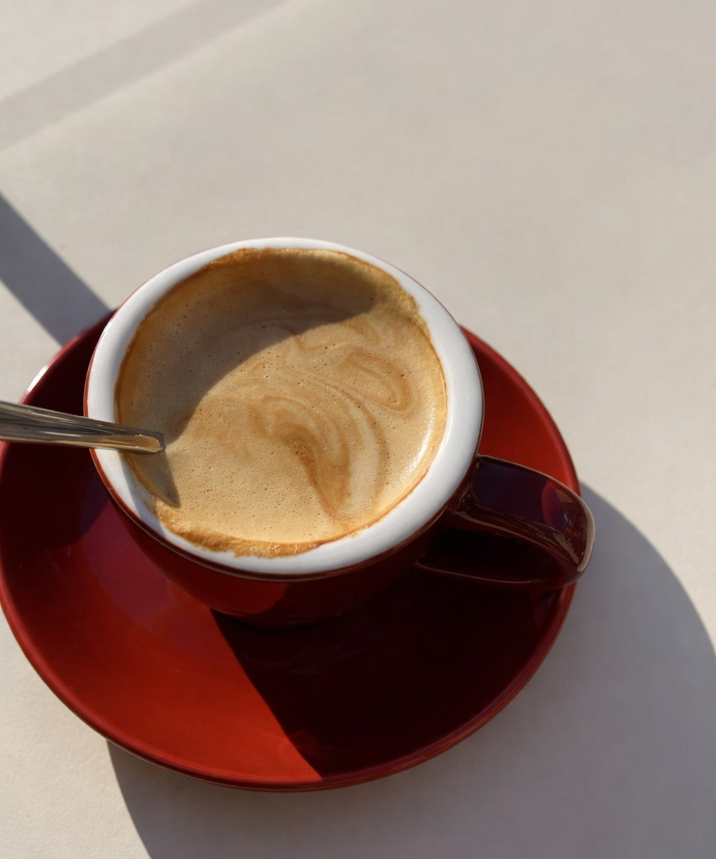 Cup of coffee with a spoon on a red saucer against a neutral background