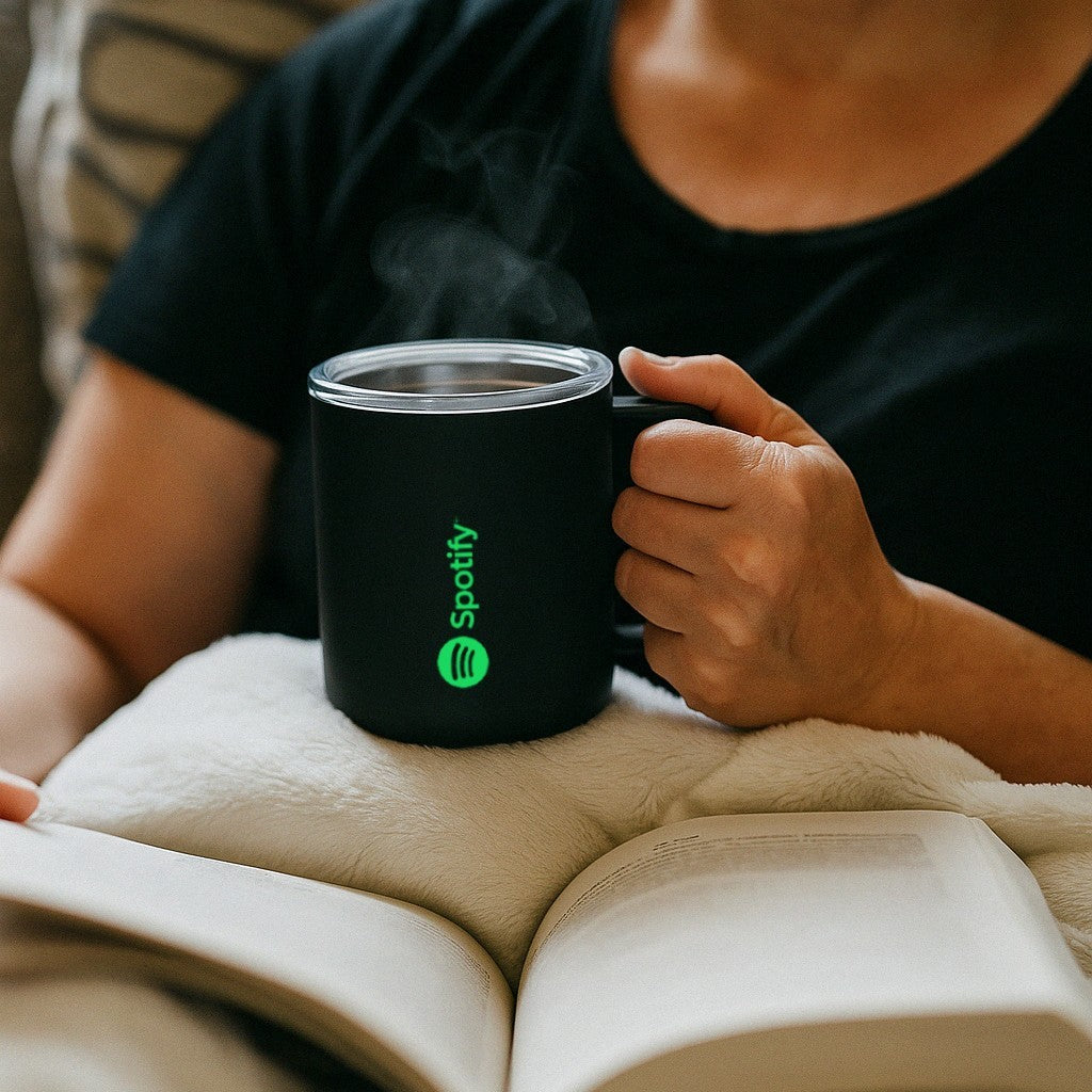 Person holding a company branded Spotify mug with a book open on their lap