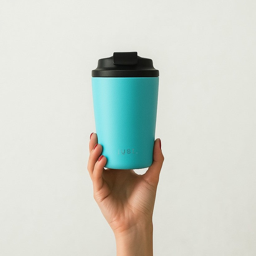 Hand holding a blue reusable coffee cup with a black lid against a light gray background