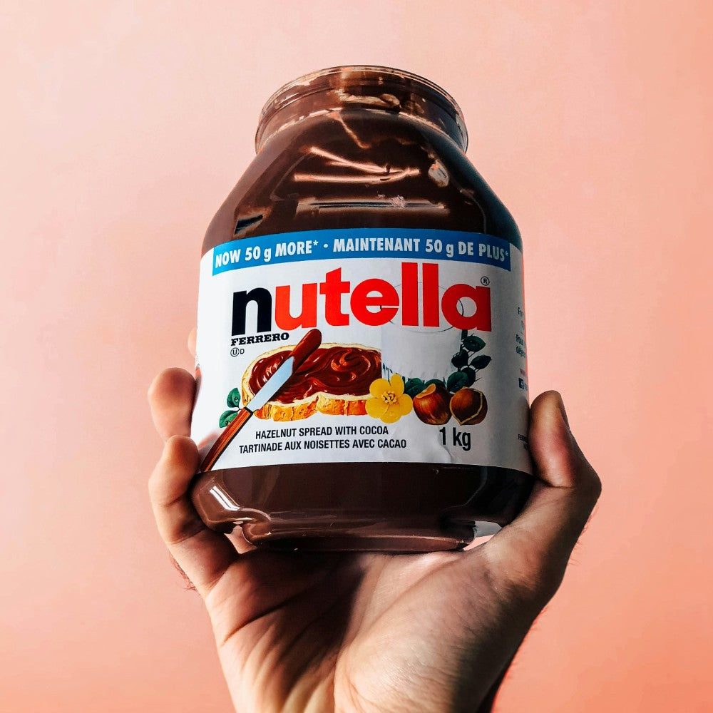 Hand holding a jar of Nutella against a pink background