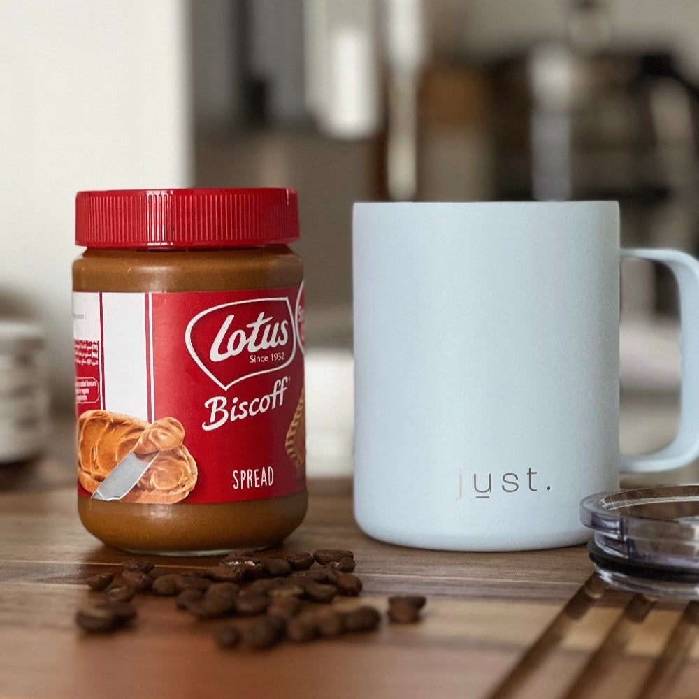 Jar of Lotus Biscoff spread with a white metal coffee mug on a wooden surface.