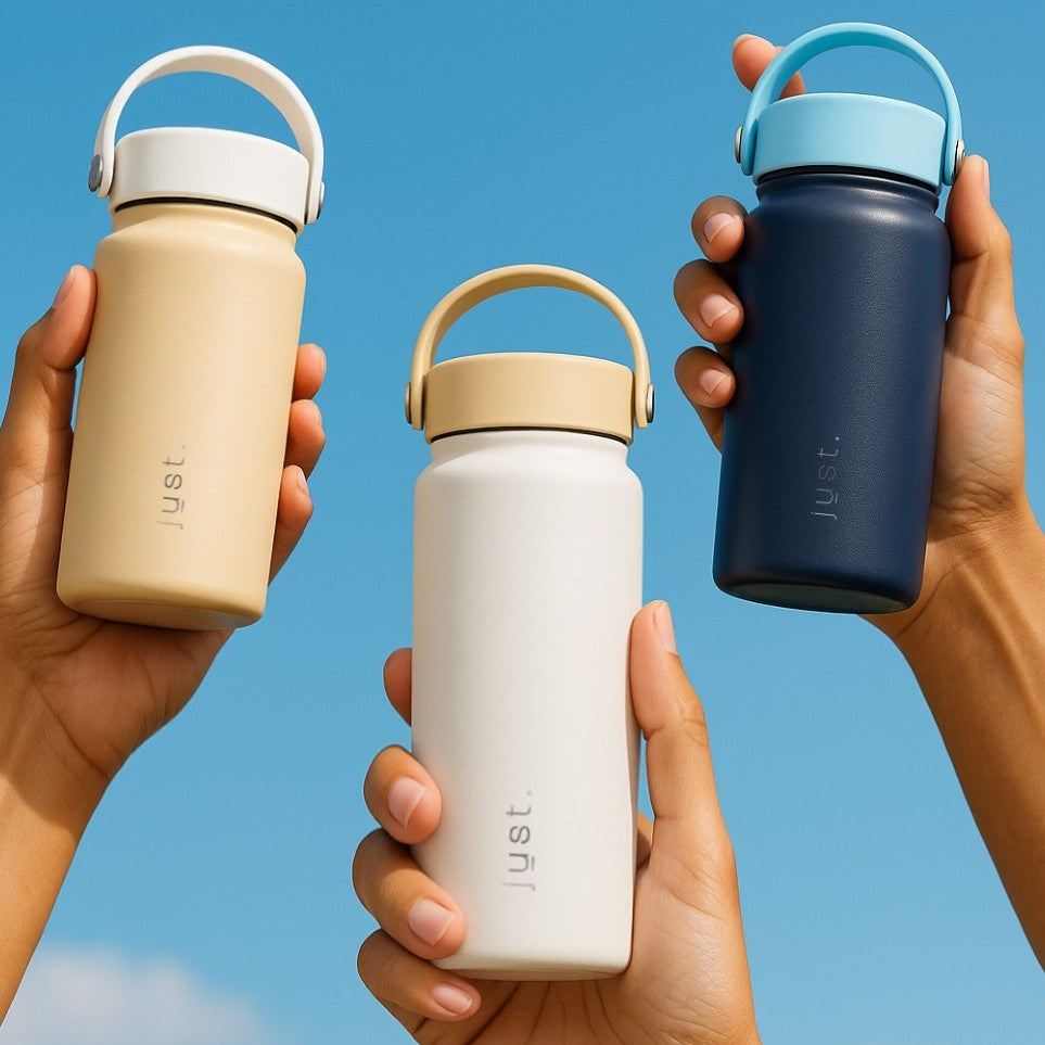 Three hands holding reusable water bottles with 'Just' branding against a blue sky.
