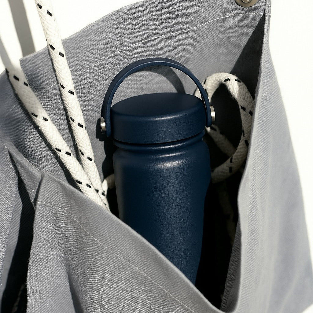 Nomad stainless steel water bottle in dark blue inside a canvas bag