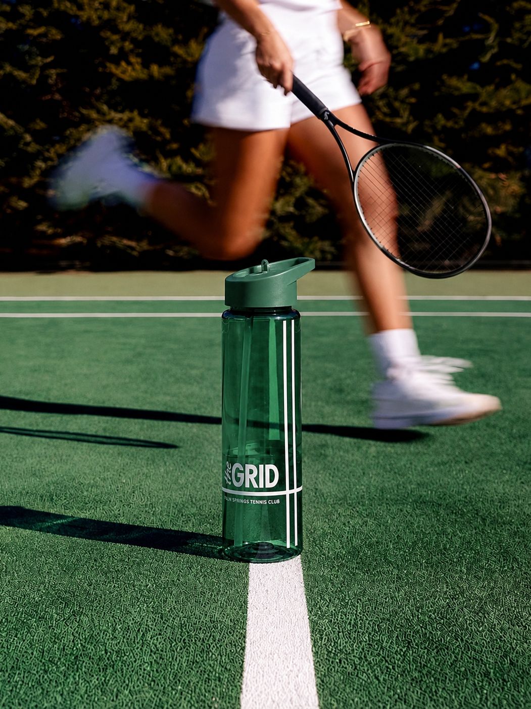 green recycled plastic water bottle with straw lid and custom logo on a tennis court