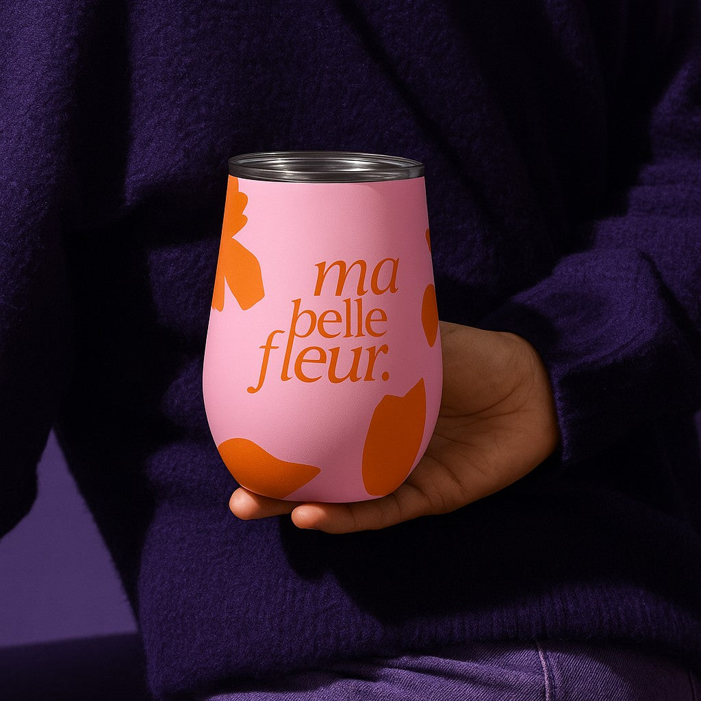 Person holding a pink tumbler cup with orange floral designs and 'ma belle fleur' text.