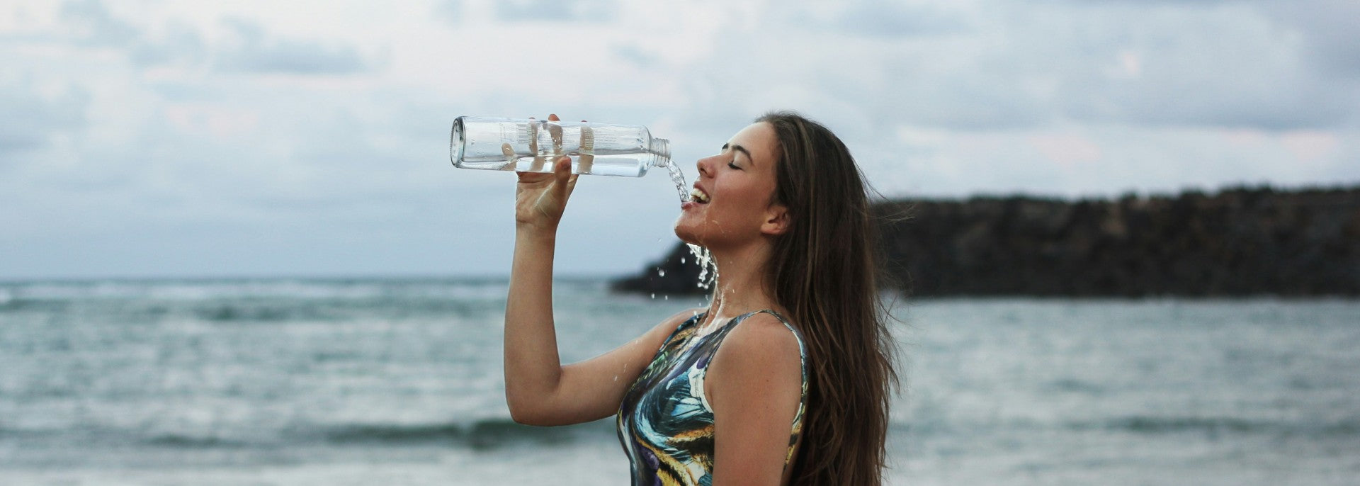 Lady on the beach drinking from a glass bottle