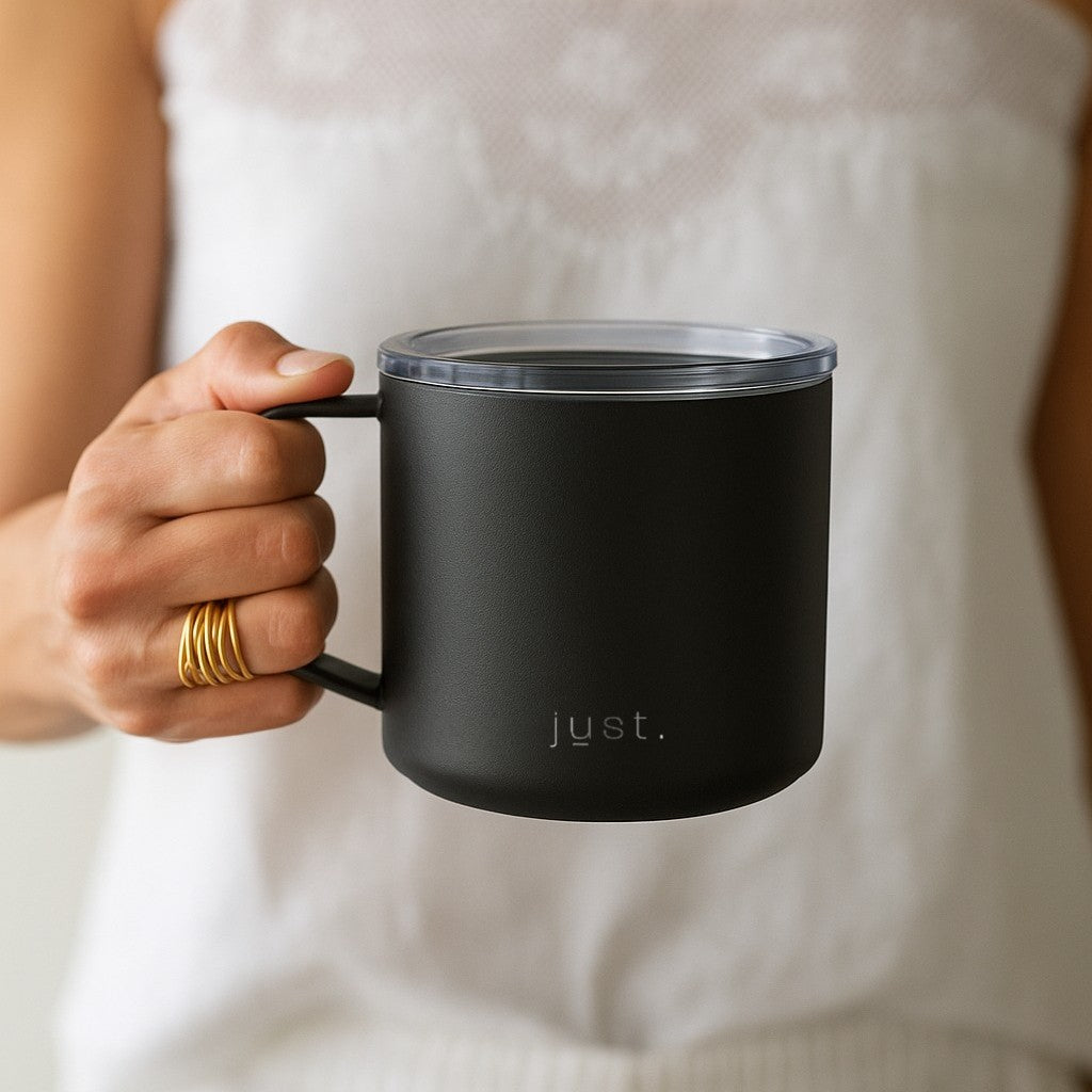Person holding a black travel mug with Just Bottle branding against a neutral background 