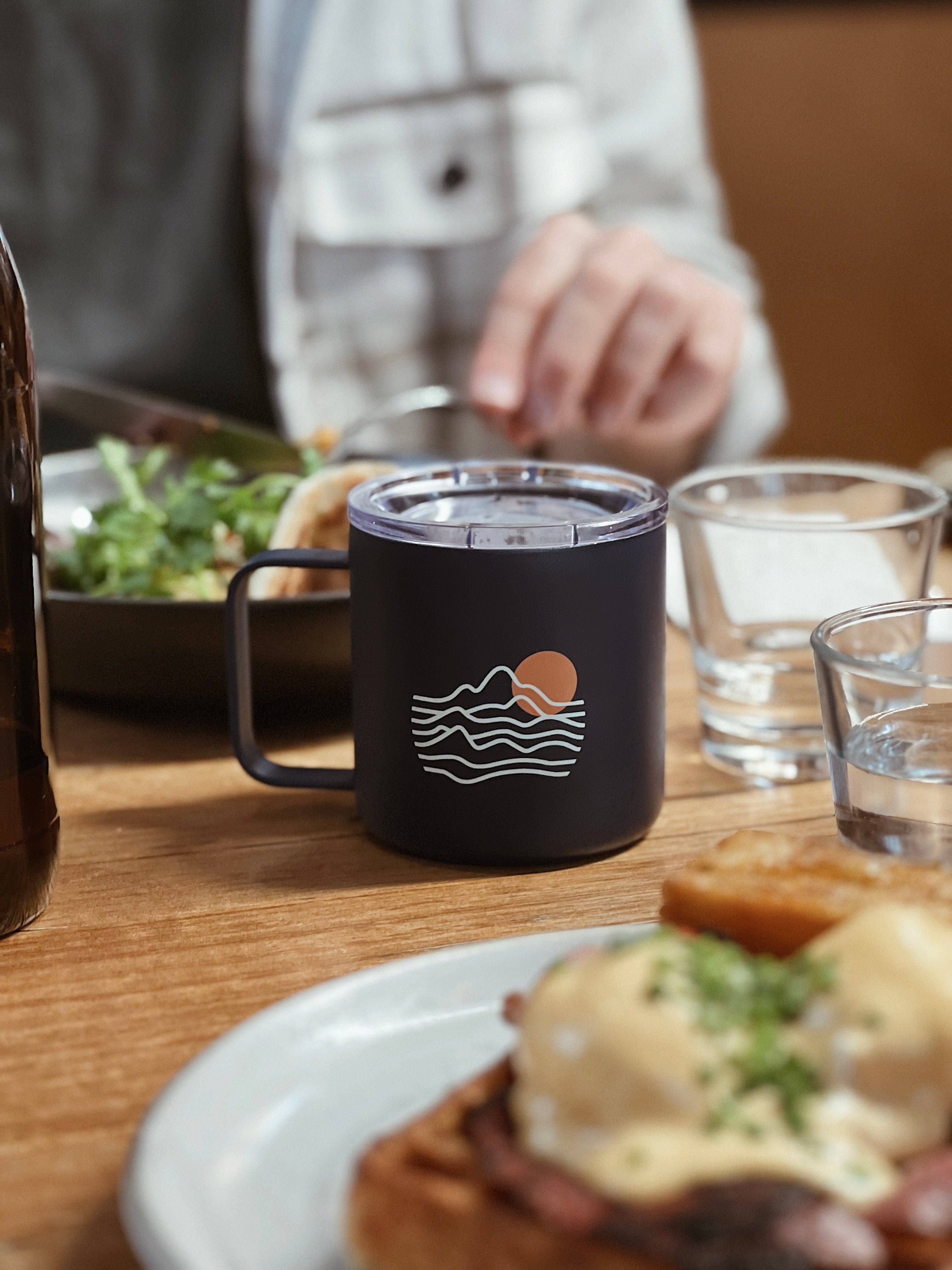 blue stainless steel co brand custom logo mug on a table next to a glass of water