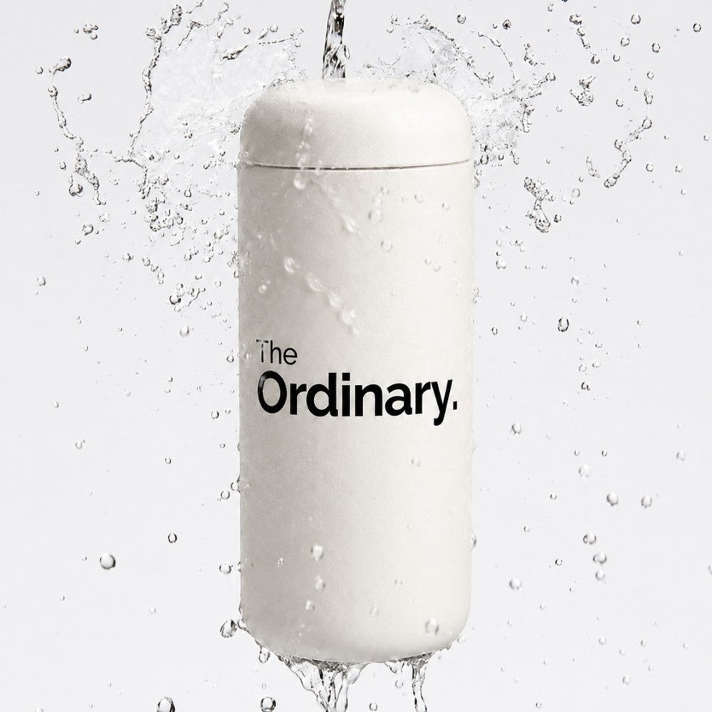 Custom leakproof tumbler in white with "The Ordinary" logo printed in black, on a water splash background