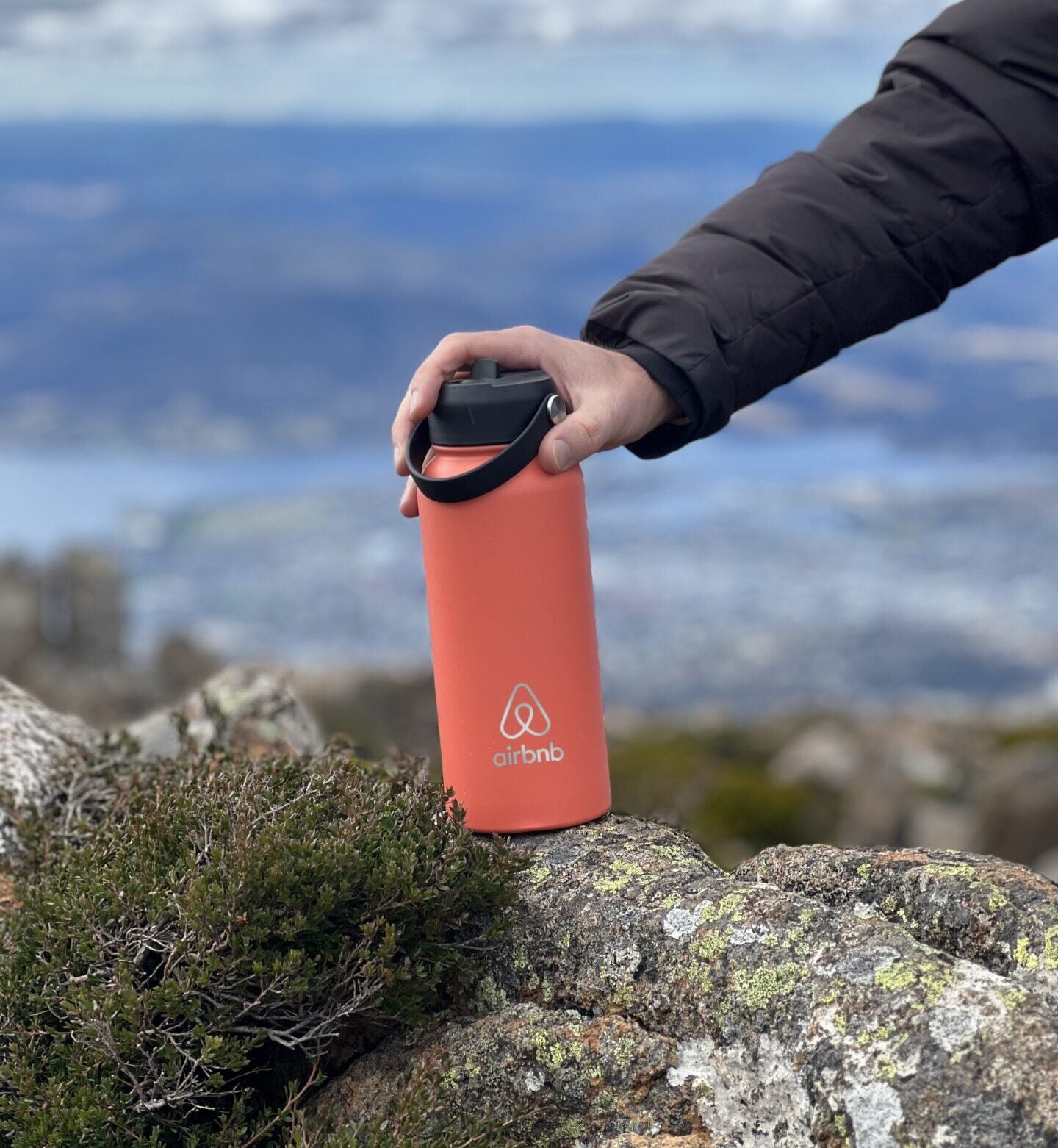 orange 1 litre metal custom branded water bottle with laser engraved logo on a rock