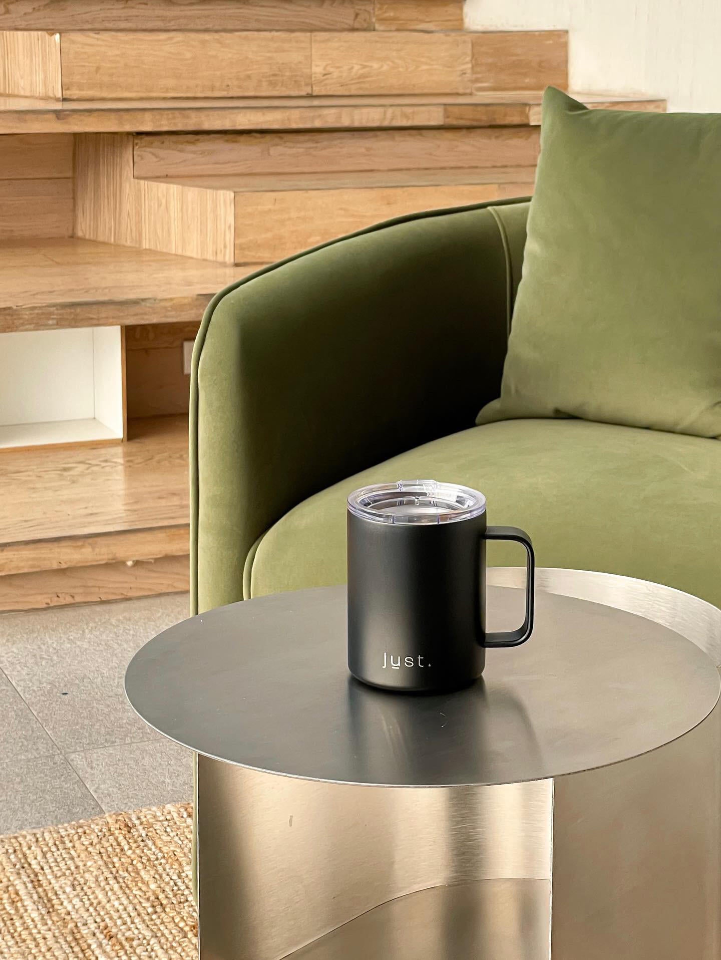 black travel mug on coffee table next to a green sofa