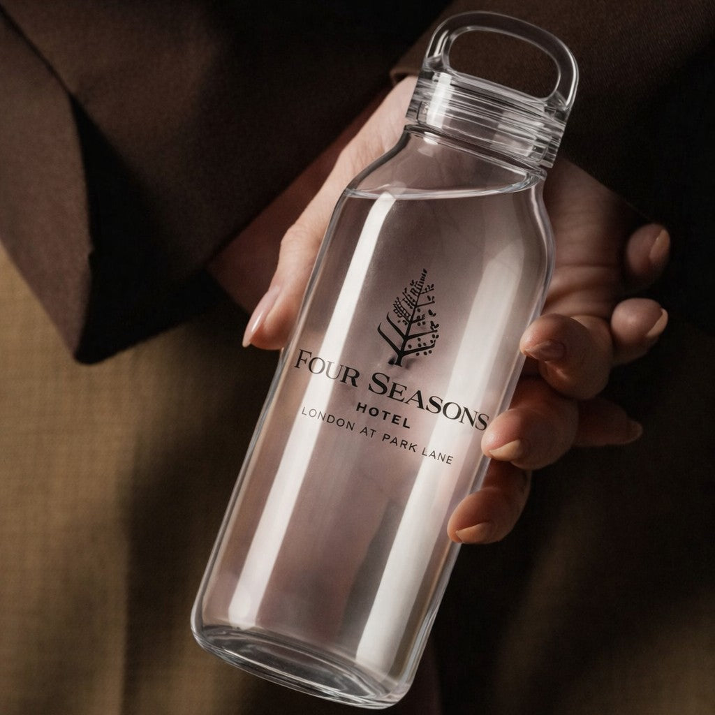 Clear glass water bottle with Four Seasons Hotel logo held by a person