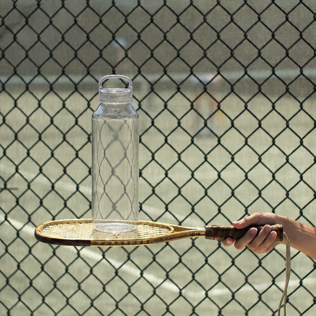 Large clear glass water bottle on a tennis racquet