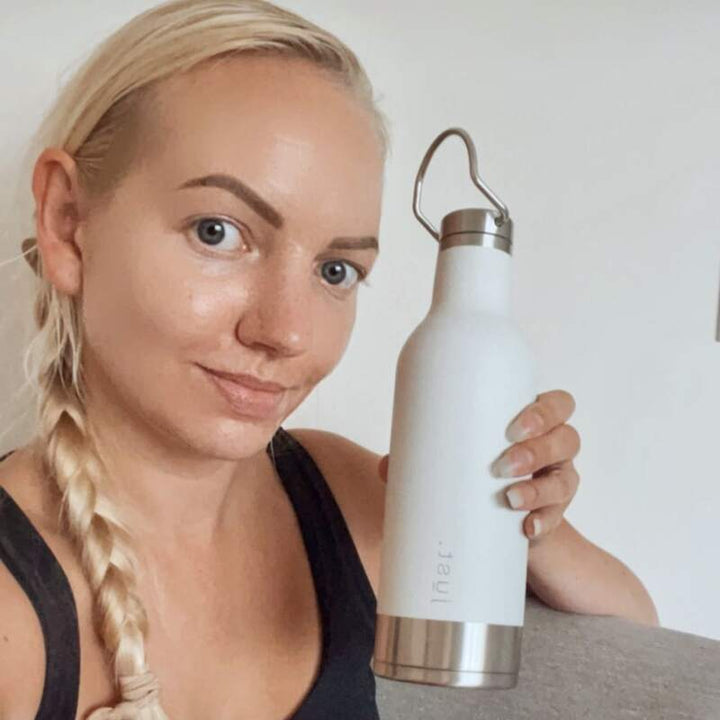 Aggie.wanderlust holding her glacier white lightweight reusable water bottle 