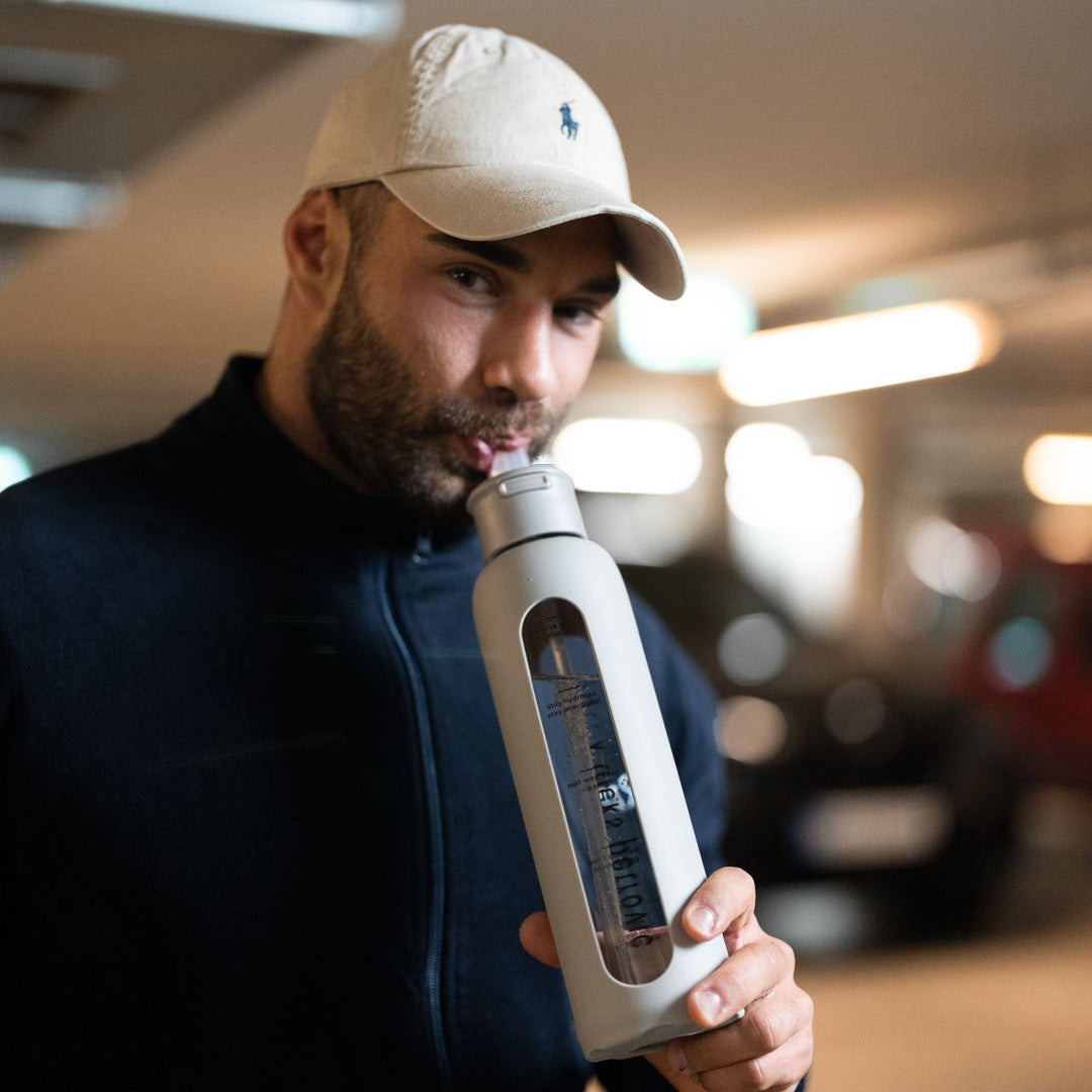 man drinking from glass water bottle with straw lid