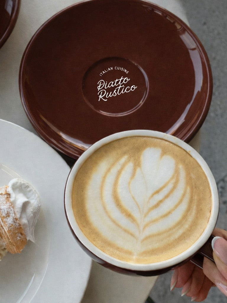 Cappuccino with latte art held by a hand with a custom branded saucer underneath