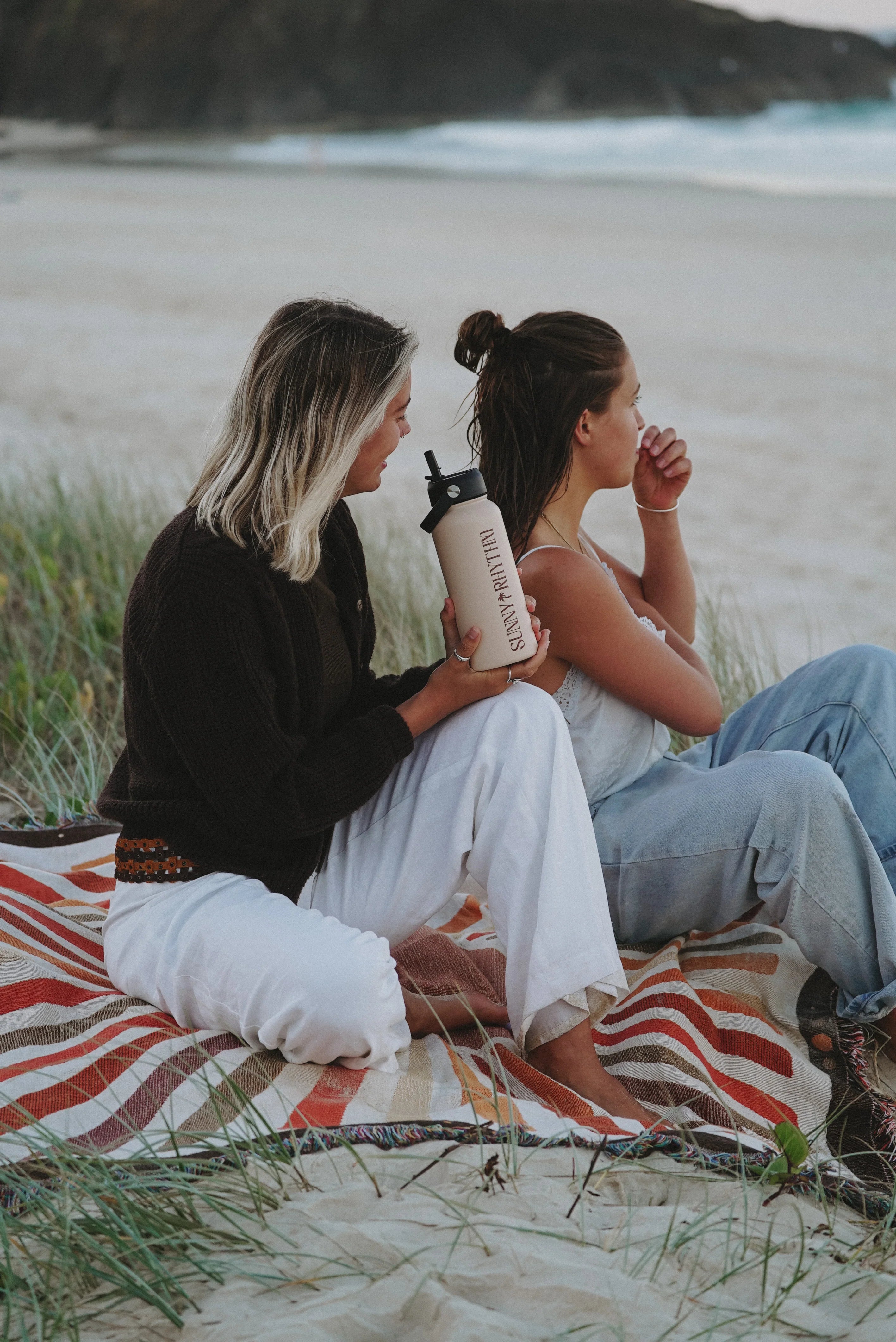 two people sat on a towel holding a beige coloured 1 litre stainless steel water bottle with a custom printed logo