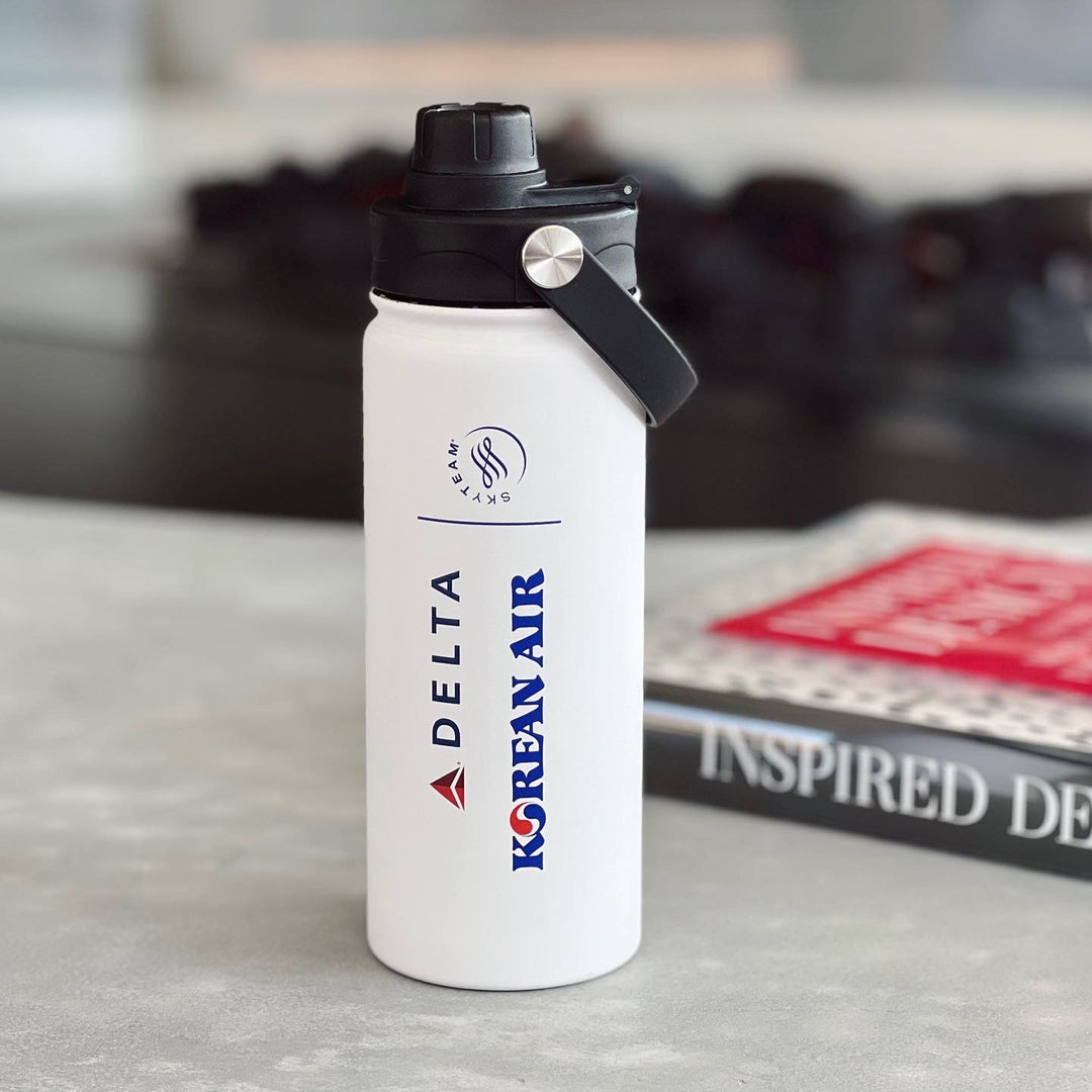 white stainless steel bottle with Delta, Korean Air and Sky Team logo next to the magazine