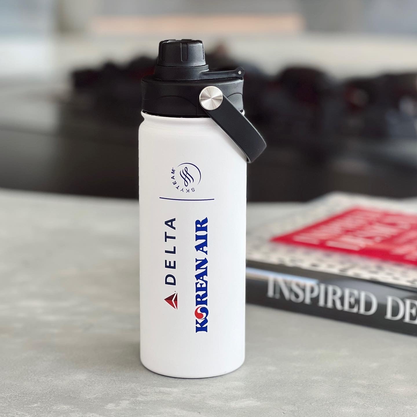 white stainless steel bottle with Delta, Korean Air and Sky Team logo next to the magazine