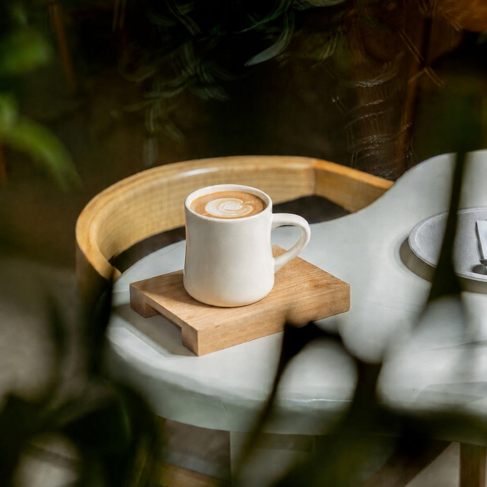 Diner mug with a coffee drink on a wooden coaster on a white chair with a blurred background