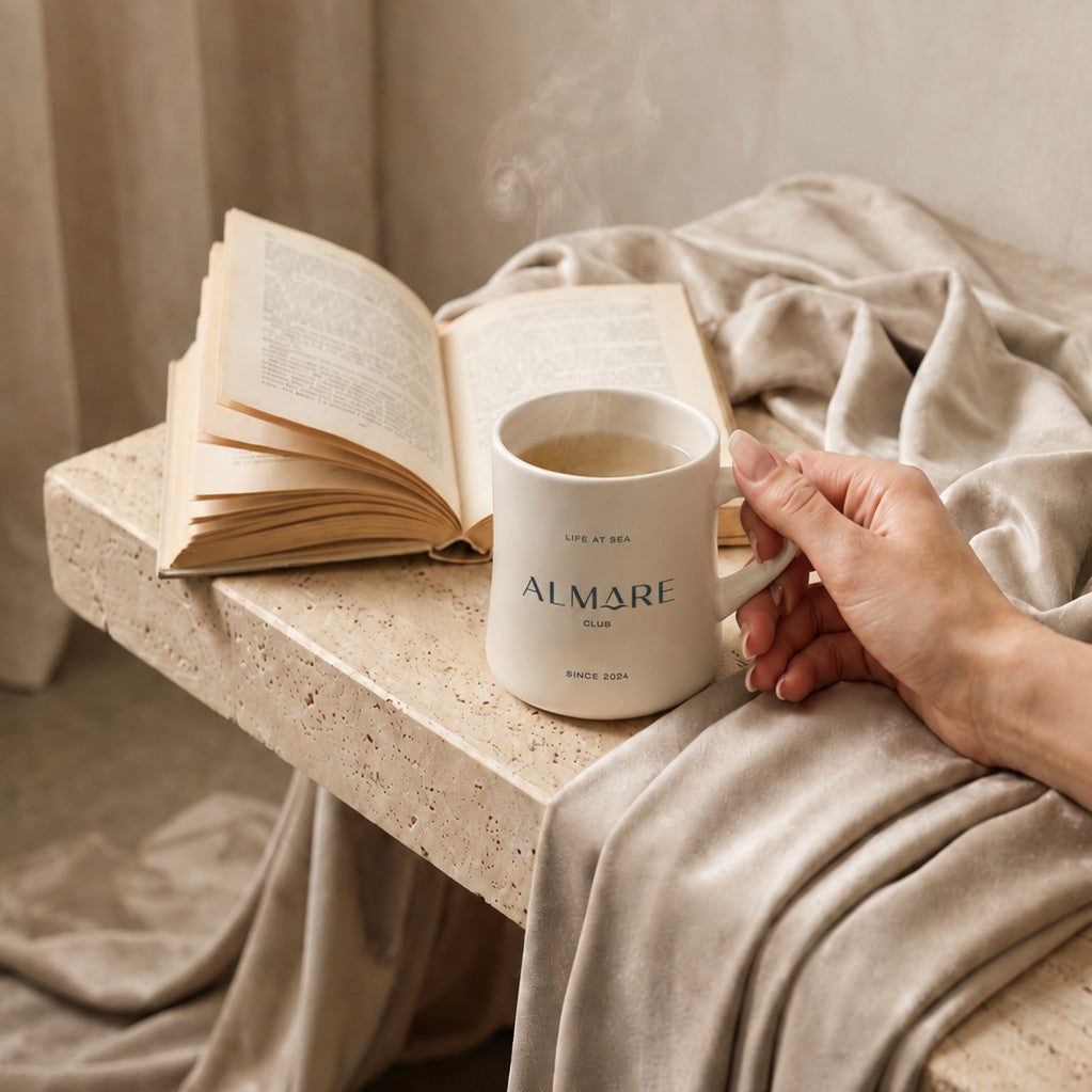 Person holding a classic diner mug with custom branding next to an open book on a stone surface with a soft, neutral background.