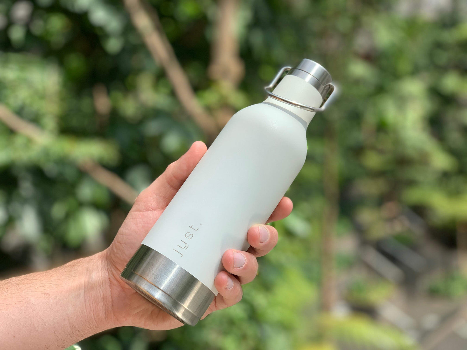 White reusable water bottle held in hand with trees in background