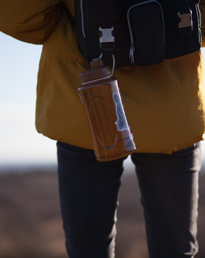 glass water bottle hanging from backpack in nature