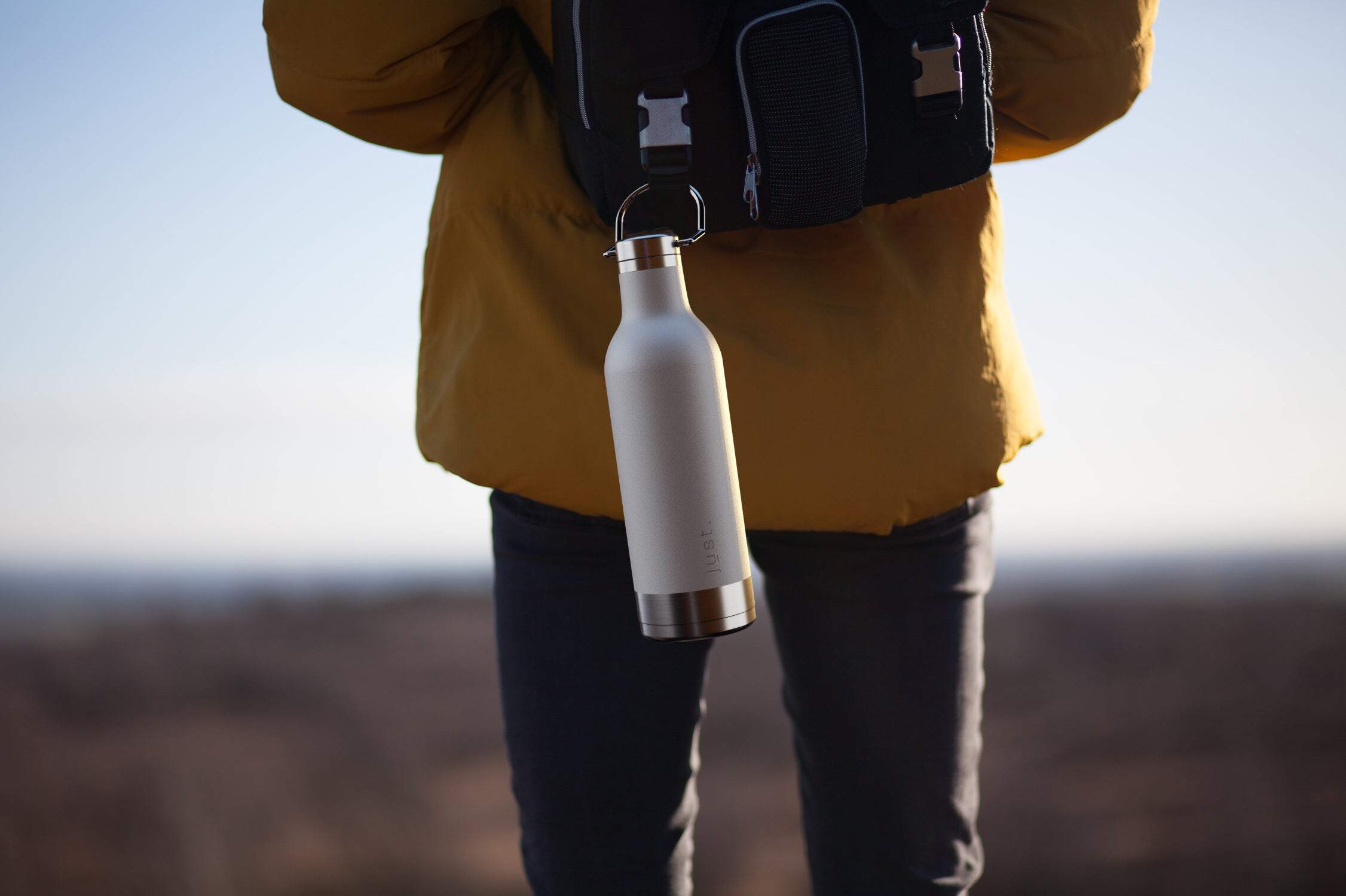 Man hiking with white water bottle attached to black backpack wearing a yellow jacket