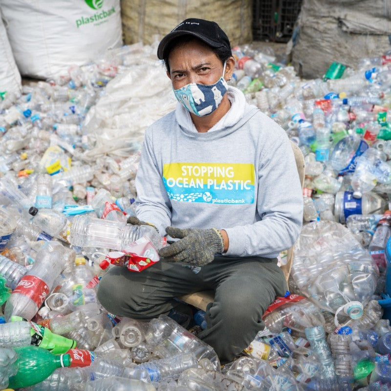 Person sitting amidst a pile of plastic bottles with 'Stopping Ocean Plastic' text on a shirt.