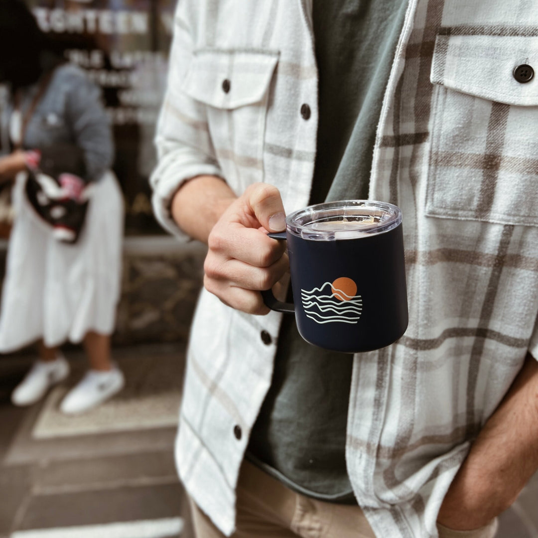 Just Bottle Slow Sip mug held in hand with cafe behind