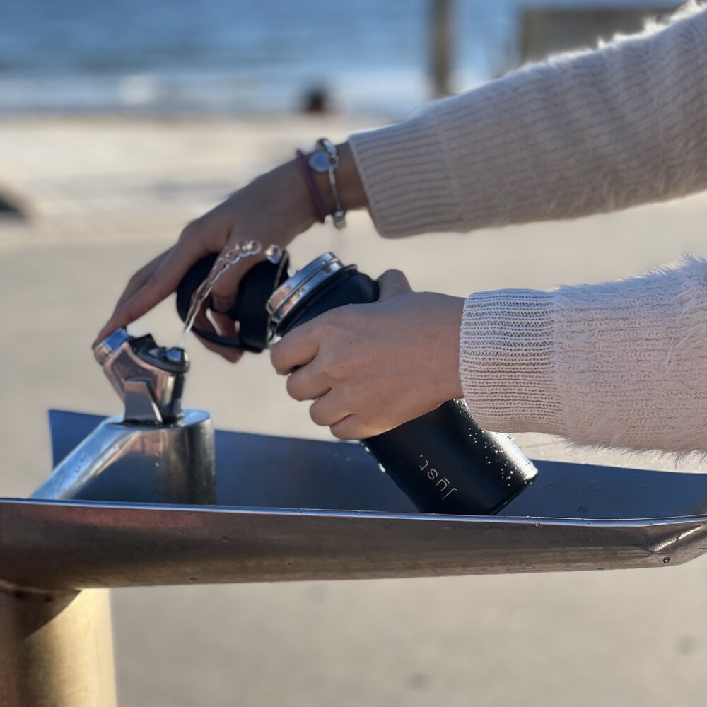 black stainless steel water bottle being filled at a water station at the beach