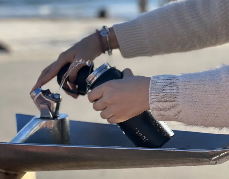 black water bottle being filled at a water fountain