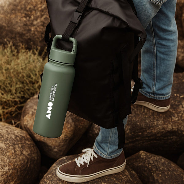 Person holding a green custom logo carabiner water bottle with a backpack on a natural background