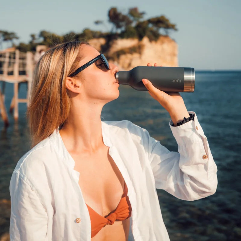 lady drinking from grey reusable water bottle near the sea