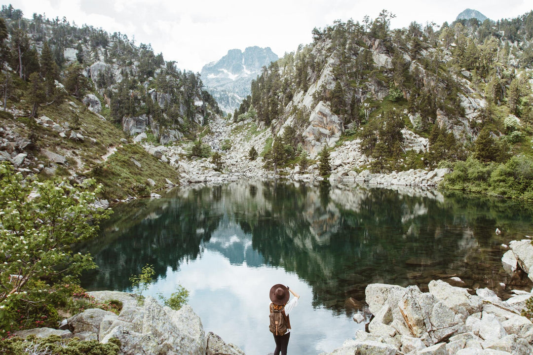 traveller hiking standing at green lake looking at rocky mountains with pine trees