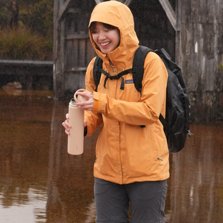 hiker holding a 750ml (25 oz) reusable water bottle in beige - stainless steel durability