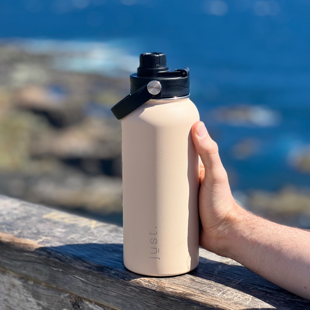 sand colour Just Bottle sustainable stainless steel reusable water bottle with ocean in the background