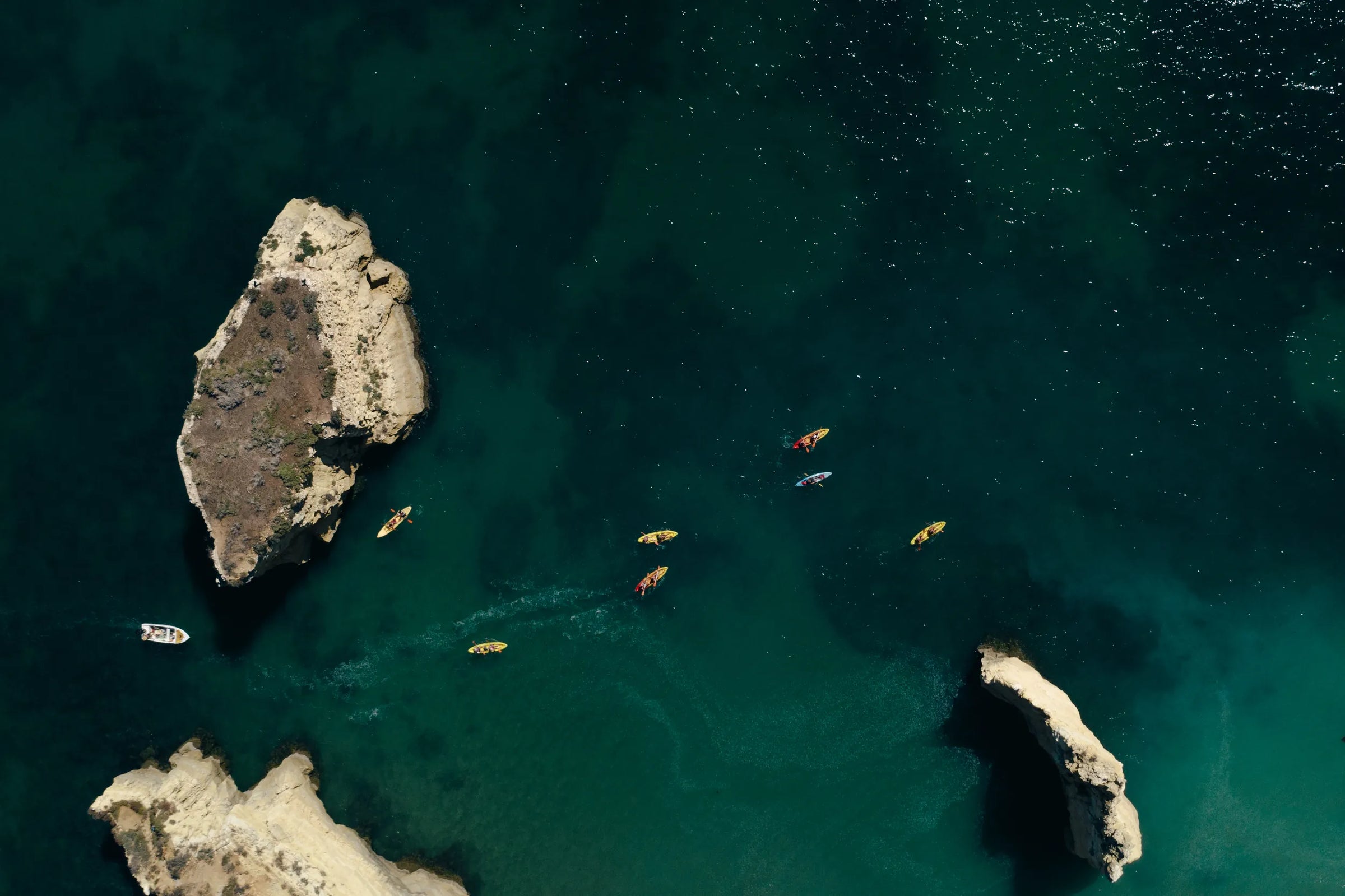 people kayaking around rocks in the ocean
