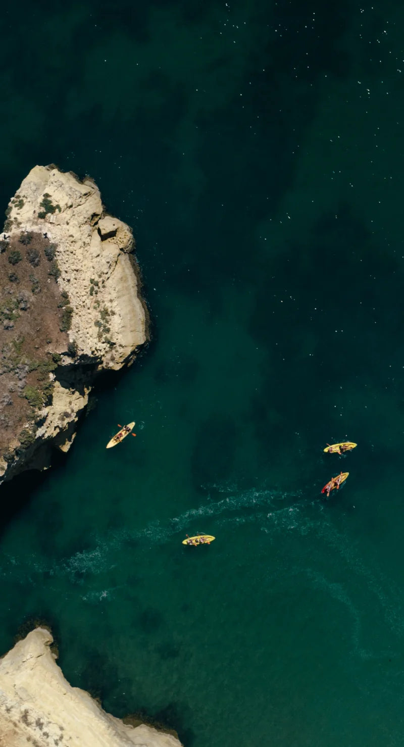people in the sea kayaking around rocks