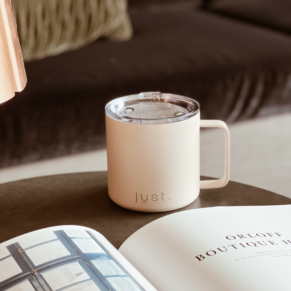 Pink stainless steel insulated mug on table with book 