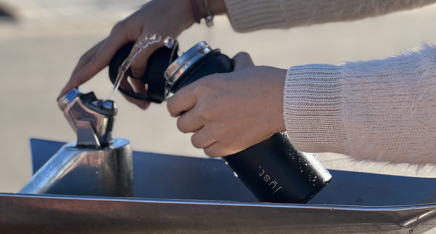 black stainless steel reusable water bottle being refilled at a water fountain