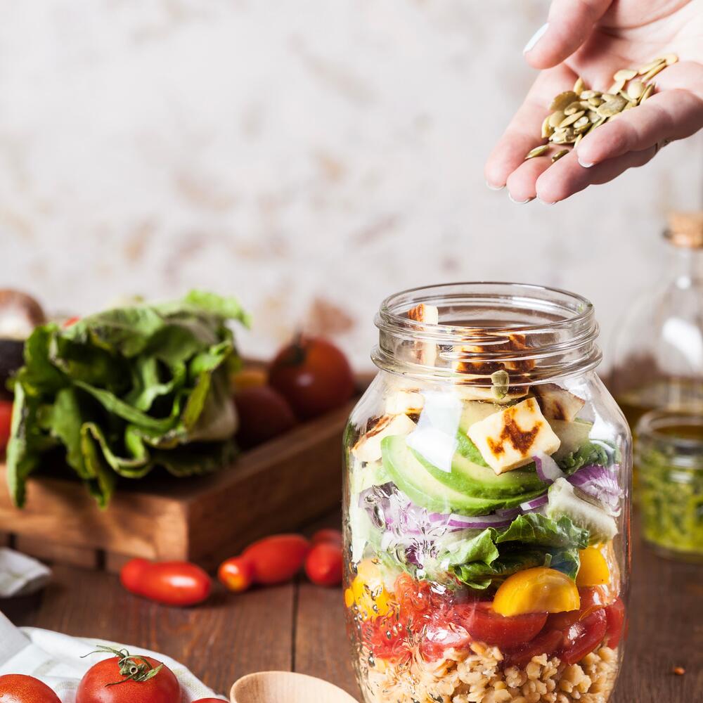 vegetables and plants inside of a glass jar on a brown table